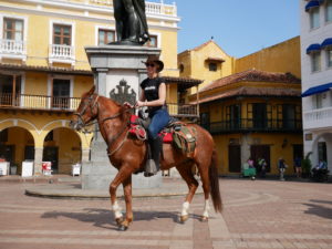 Caroline in a block t-shirt and jeans riding a brown Horse